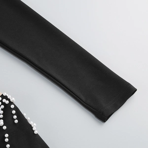 Détail d'une robe noire à manches longues avec ornements décoratifs de perles blanches