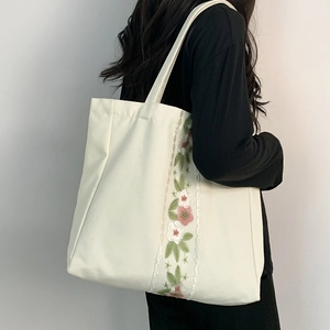 Dettaglio del ricamo floreale su una borsa tote in tela color crema indossata da una modella