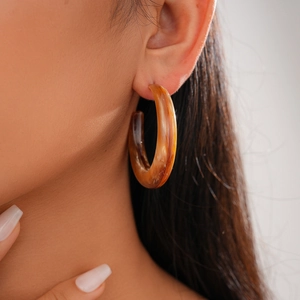 Close-up of amber resin C-shape hoop earring with tortoiseshell pattern on model