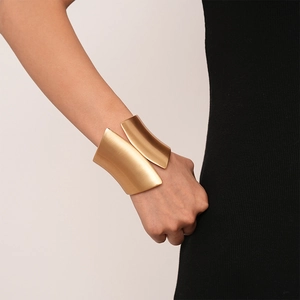 Macro detail of wide gold metal cuff with textured brushed finish and layered design