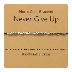 Detail of Morse code bracelet featuring silver beads on black cord with Kraft paper card