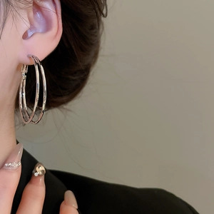Silver-colored double hoop earrings with a minimalist twisted design worn by a model