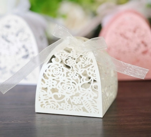 Macro view of white laser-cut wedding candy box with elegant floral hollow and ribbon bow