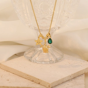 Detail of gold necklace featuring turtle, star and green teardrop gemstone pendants