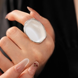 Close-up of minimalist white oval resin ring with silver metal band on black background