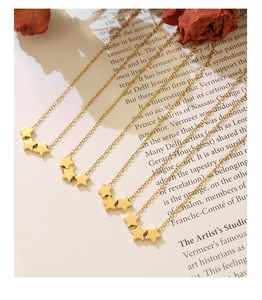 Détail de trois pendentifs étoiles dorées sur une chaîne fine avec une finition polie