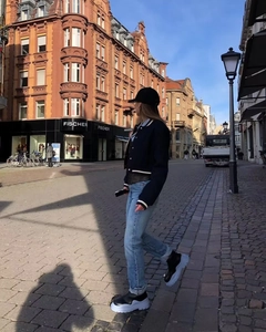 Street style view of a black baseball jacket paired with blue jeans and two-tone boots