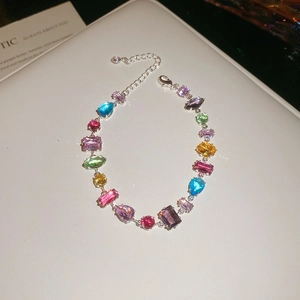 Detail of silver bracelet with multi-colored crystals and heart charm on white surface