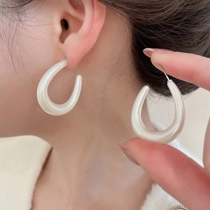 Detail view of pearl white U-shaped acrylic earrings with a glossy iridescent shell finish