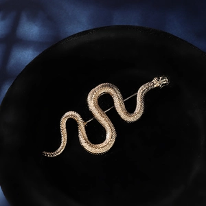 Close-up of golden snake brooch with detailed scale texture on black velvet background