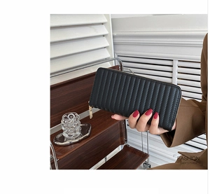 Detail of a black long zipper wallet featuring quilted vertical stripes and gold hardware