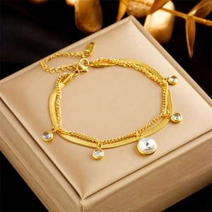 Detail of layered gold bracelet featuring snake chain with sparkling round zircon charms