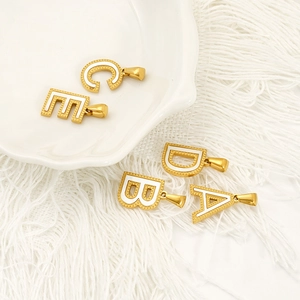 Gold plated stainless steel alphabet pendants with white enamel on a ceramic tray