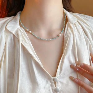 Close-up of gold-plated necklace with light blue beads and irregular white pearls