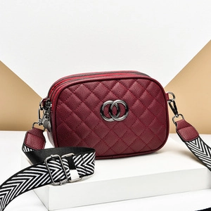 Close-up of wine red quilted leather bag with striped strap and metallic double ring buckle