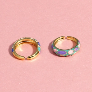 Vue détaillée de deux bagues émaillées dorées avec incrustations colorées sur fond rose