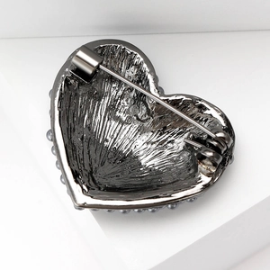 Elegant heart-shaped brooch with pearls and dark metal plating on a white platform