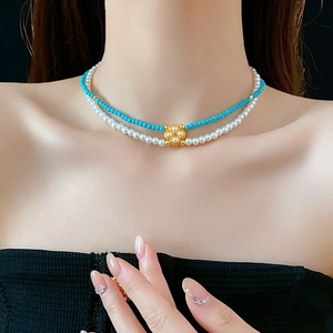 Dettaglio collana a due strati con perle bianche, perline verdi e ciondolo a quadrifoglio