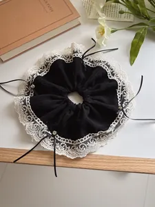 Detail of black bow hair scrunchie with cream lace trim and crystal accents