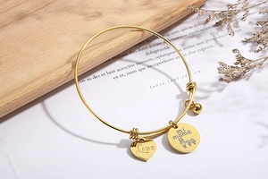 Close-up of golden expandable bracelet with Love heart and mi mama charms on wooden background
