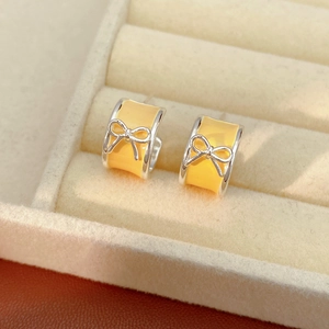 Detail of yellow enamel bow C-shaped stud earrings in a white velvet jewelry box