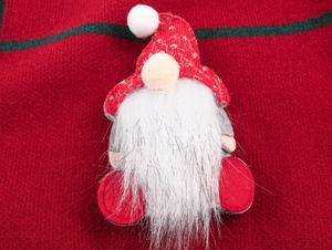 Gros plan d'un nain de Noël avec bonnet tricoté rouge et barbe en fourrure sur fond rouge