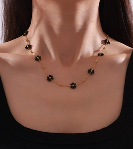 Gros plan du collier en chaîne dorée avec breloques fleurs en pierre noire sur un modèle