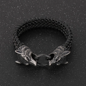 Macro detail of antique silver double wolf heads on black braided leather men's bracelet