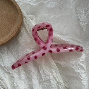 Detailed view of a pink hair claw clip with dark pink polka dots on a white background