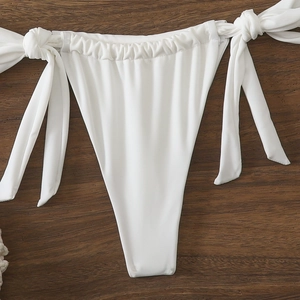 Dettaglio dello slip bikini bianco con laccetti e trama a costine su sfondo in legno