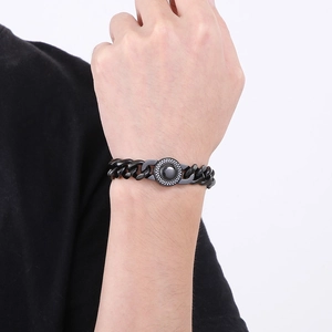 Detail of a black Cuban chain bracelet with a stone-inlaid circular charm on a male wrist