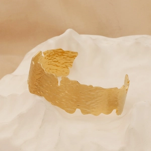 Detailed view of wide gold hammered cuff bracelet with irregular wave edges on stone base