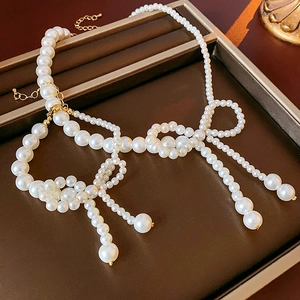 Dettaglio di una collana di perle bianche con fiocco e chiusura dorata su un vassoio