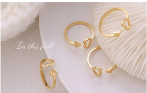 Detailed view of adjustable 18K gold plated arrow and heart rings on textured fabric
