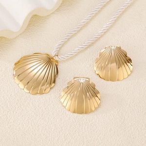 Golden seashell jewelry set with pendant necklace and earrings on white textured surface