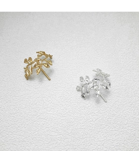 Detail view of leaf-shaped hair pins in gold and silver finishes on a textured background