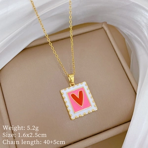 Detail view of a square gold necklace with pink enamel and red heart in a jewelry box