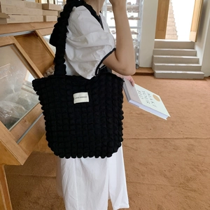 Dettaglio della borsa tote nera con trama popcorn e patch logo in un ambiente accogliente