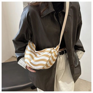 Detail of a large yellow and white striped crossbody hobo bag on model in leather jacket