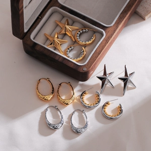 Detail of minimalist star-shaped earrings and textured gold hoops in a wooden jewelry box