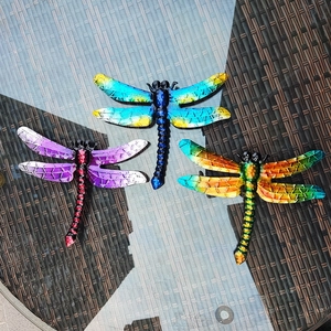 Three colorful metal dragonfly wall decors with gradient paint on a glass surface