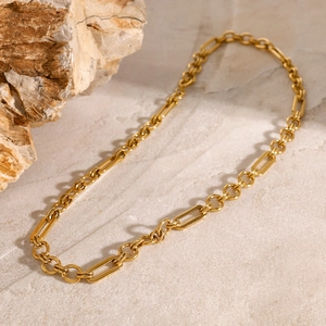 Gold plated stainless steel necklace with textured links on a beige stone surface