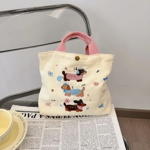 Détail du sac en velours côtelé avec broderie de chien et anses roses sur des magazines