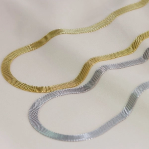 Detailed close-up of gold and silver mesh choker necklaces on soft beige satin fabric