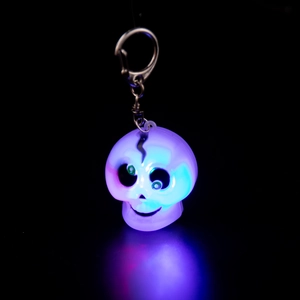 Close-up of glowing purple skull keychain with blue-purple LED light on black background