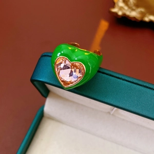 Detailed macro view of heart-shaped green enamel ring with pink zircon on a jewelry box