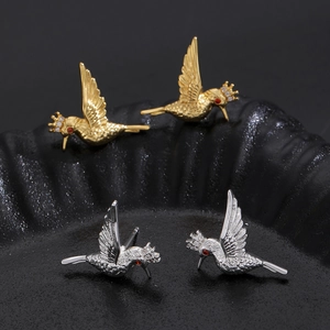 Macro shot of hummingbird stud earrings in gold and silver with red zircon eyes