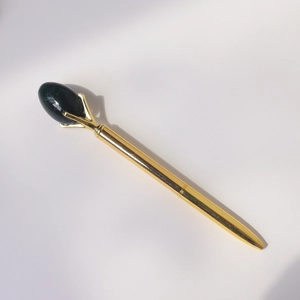 Detail of a golden metal ballpoint pen featuring a claw-set dark green gemstone topper