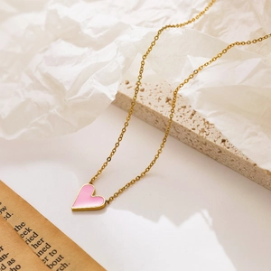 Detail of pink enamel heart pendant with golden chain on elegant stone aesthetic background