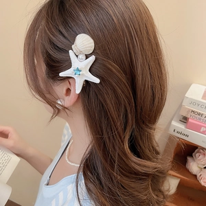Detail view of starfish shell and pearl hair clip worn on model for seaside vacation style